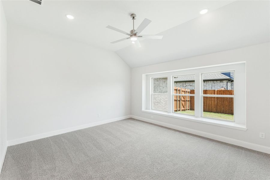 Empty bedroom with vaulted ceiling, ceiling fan, gray carpet, and large window overlooking backyard fence Empty bedroom with vaulted ceiling, ceiling fan, gray carpet, and large window overlooking backyard fence