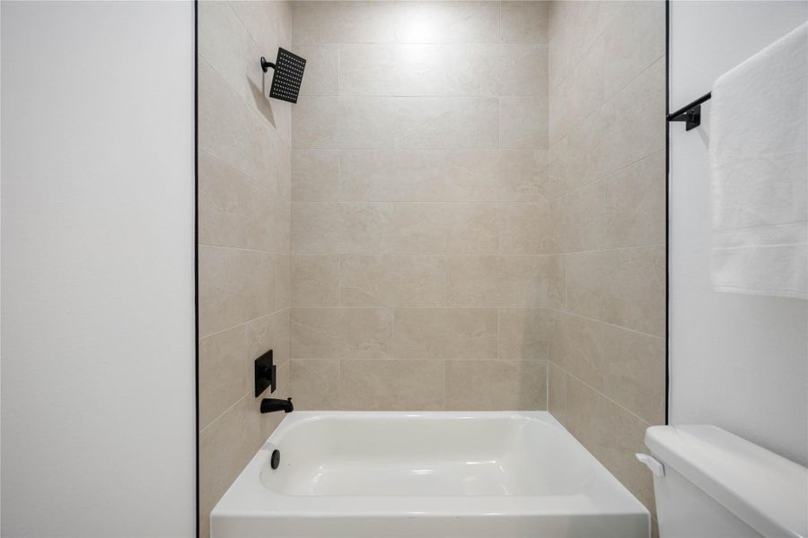 A modern shower-tub combo features large beige wall tiles and matte black fixtures for a sleek, contemporary look.