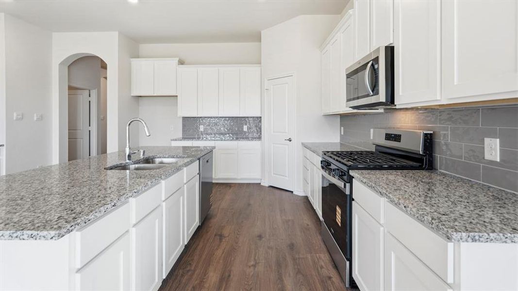 The kitchen features white cabinetry, granite countertops, stainless steel appliances, a grey subway tile backsplash, and wood-style flooring The kitchen features white cabinetry, granite countertops, stainless steel appliances, a grey subway tile backsplash, and wood-style flooring