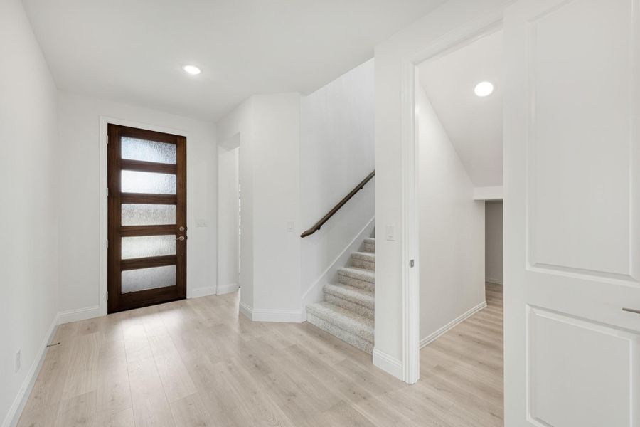 Bright entryway with wood and glass front door, staircase, and light hardwood floors