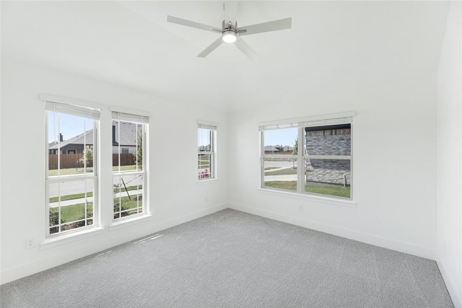 Empty bedroom with gray carpet, ceiling fan, and multiple windows with neighborhood views