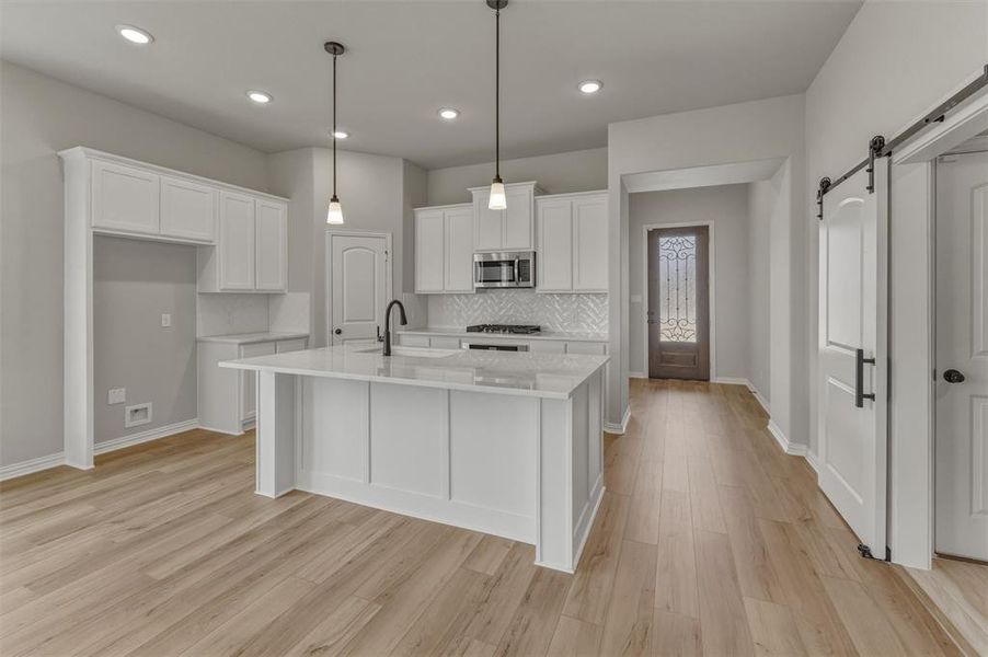Modern kitchen featuring a central island with countertop seating, white shaker cabinetry, herringbone tile backsplash, and light wood-finish flooring Modern kitchen featuring a central island with countertop seating, white shaker cabinetry, herringbone tile backsplash, and light wood-finish flooring