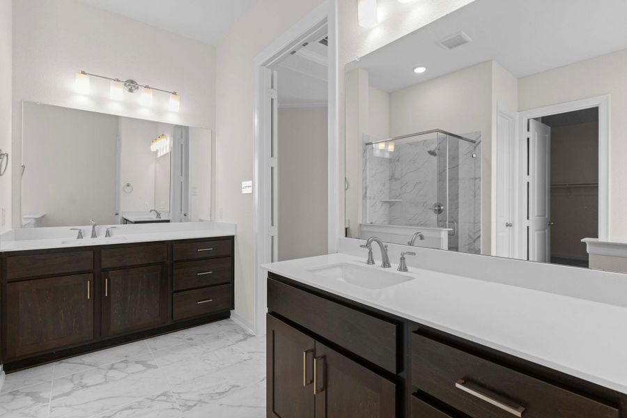 Primary bath with dual vanities, granite countertops, framed mirrors, and ample storage, combining style and everyday convenience.