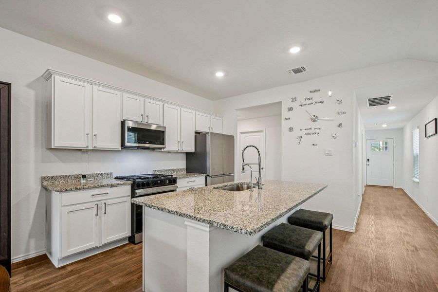 Kitchen with stainless steel appliances, white cabinets, dark wood-style floors, a breakfast bar area, and recessed lighting