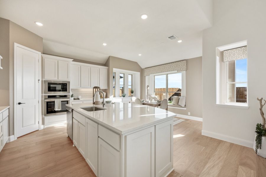 Kitchen with white cabinets, large center island, stainless steel appliances, and light hardwood floors open to living area.
