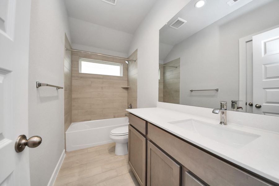 Secondary bath features tile flooring, bath/shower combo with tile surround, light stained wood cabinets, beautiful light countertop. Sample photo of completed home with similar floor plan. Actual colors and selections may vary.