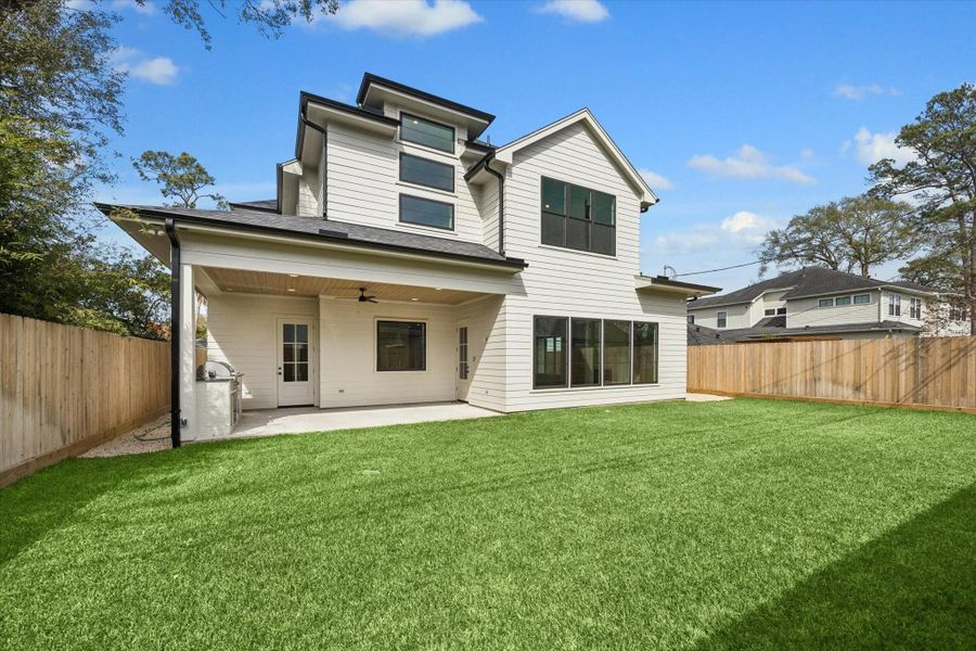 Expansive backyard pairs a covered patio and built in outdoor kitchen with a wide stretch of green space, offering room to entertain, play, or design a future pool. Clean lines and durable siding complement the modern exterior while large windows bring natural light deep into the home.