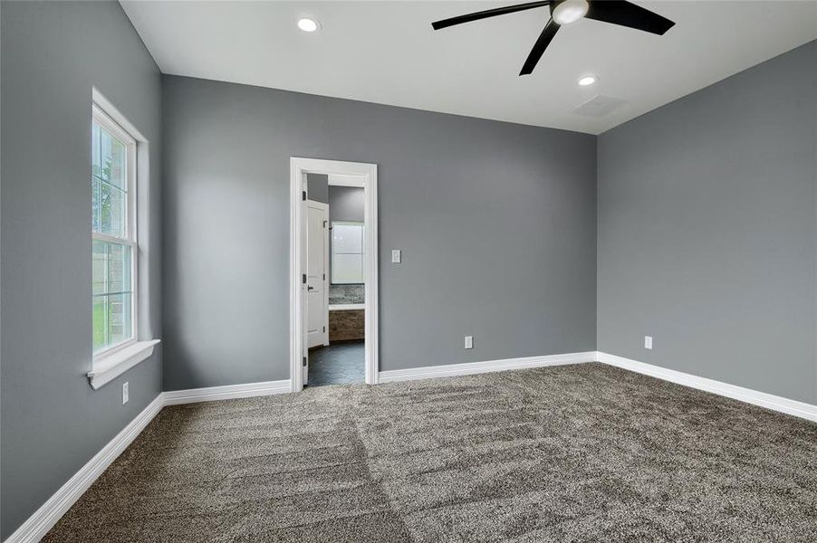 Unfurnished bedroom with ensuite bathroom, dark colored carpet, and ceiling fan