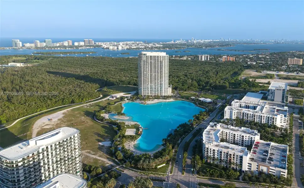 Aerial perspective of a high-rise residential complex featuring a large turquoise lagoon, landscaped grounds, multi-story buildings, and proximity to coastal water bodies