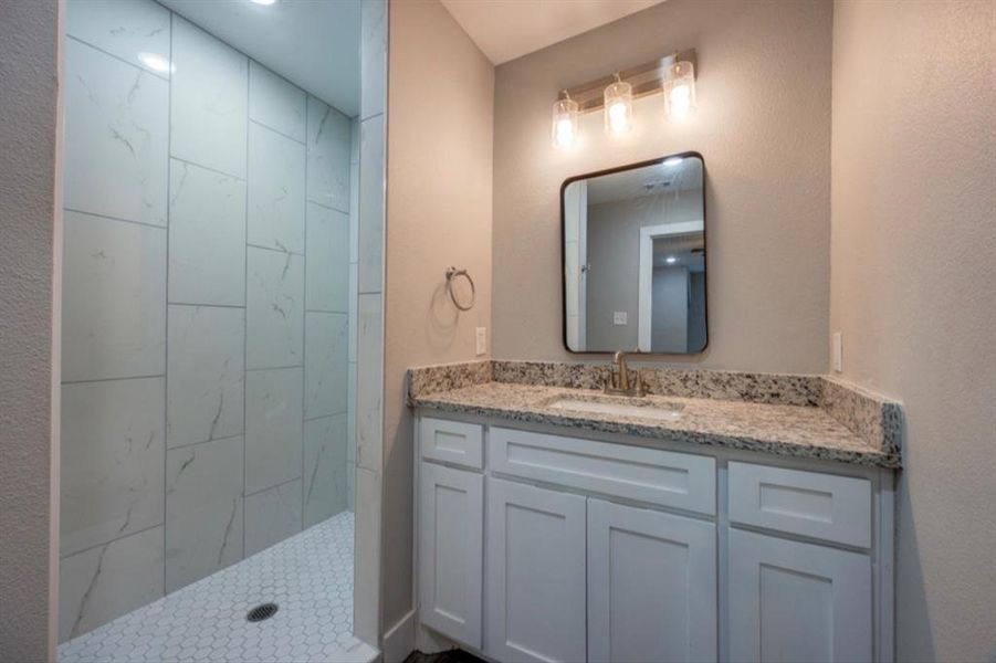 Bathroom featuring vanity, tiled shower, and a textured wall