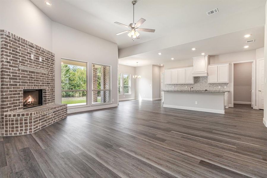 Unfurnished living room with recessed lighting, dark wood-style floors, a ceiling fan, a chandelier, and a brick fireplace Unfurnished living room with recessed lighting, dark wood-style floors, a ceiling fan, a chandelier, and a brick fireplace