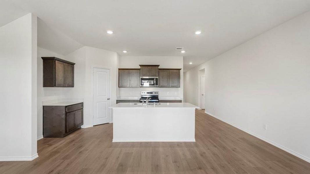 Open-concept kitchen featuring an island with a stainless steel sink, dark wood-finish cabinetry, light countertops, and wood-finish flooring