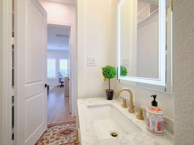 Elegant powder room with a modern countertop, gold fixtures, and a sleek illuminated mirror.
