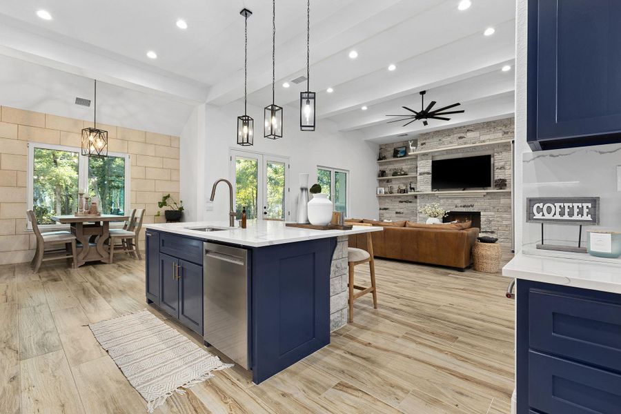Kitchen featuring blue cabinets, decorative light fixtures, beamed ceiling, light stone countertops, and a fireplace Kitchen featuring blue cabinets, decorative light fixtures, beamed ceiling, light stone countertops, and a fireplace