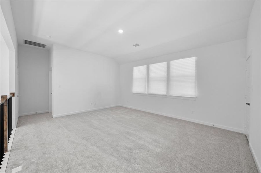 Spacious room featuring light gray carpeting, three windows with horizontal blinds, and a recessed ceiling light