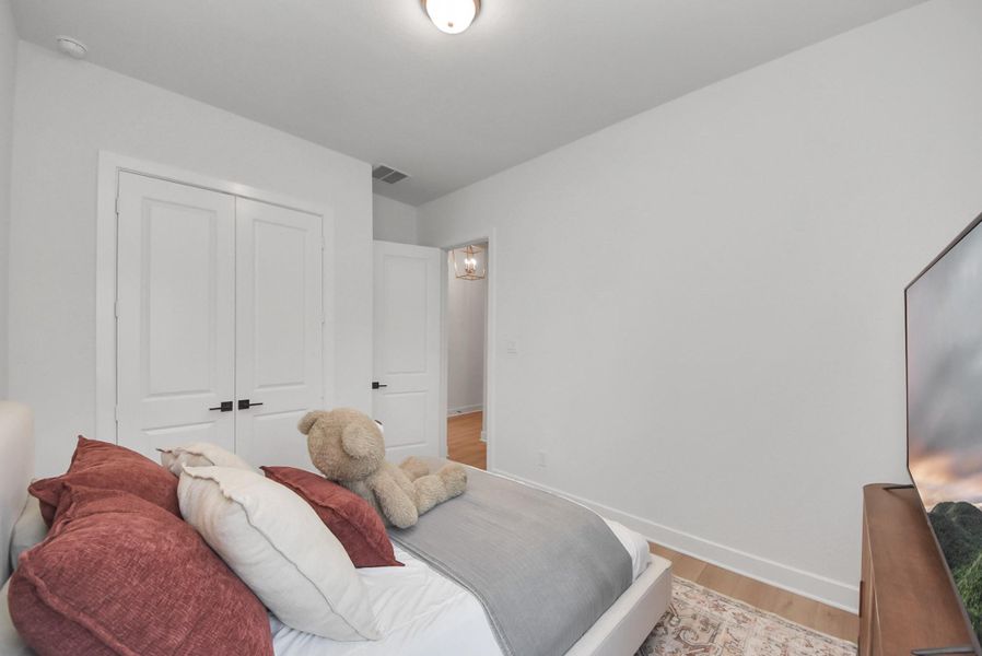 Cozy bedroom with soft neutral walls, featuring a plush bed adorned with decorative pillows and a charming teddy bear. The room offers ample storage with double doors and a warm, inviting atmosphere.