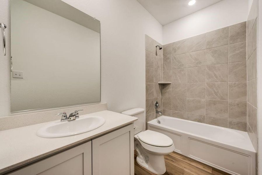 Full bathroom with tiled shower / bath combo, vanity, toilet, and wood-type flooring