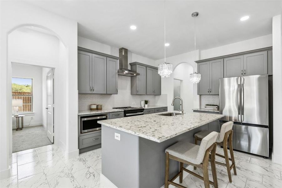 Kitchen featuring wall chimney range hood, hanging light fixtures, light carpet, stainless steel appliances, and sink