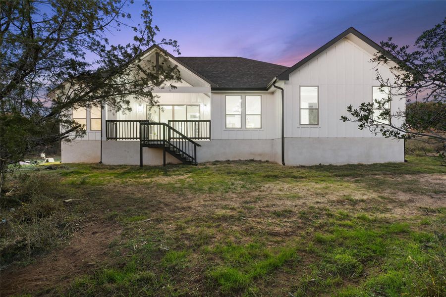 Back of property with board and batten siding, a yard, and a shingled roof