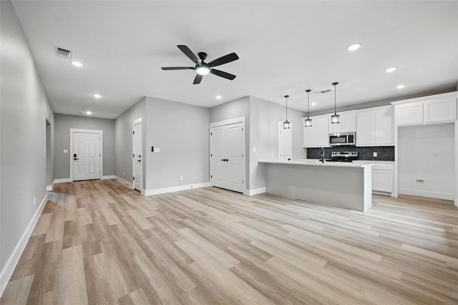 Unfurnished living room featuring recessed lighting, a sink, baseboards, a ceiling fan, and light wood-style floors