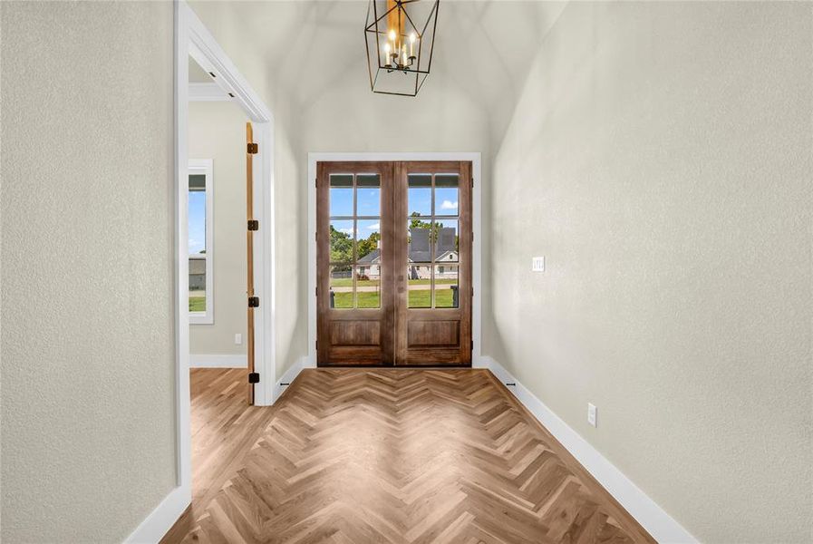 Foyer featuring a textured wall, a chandelier, and french doors