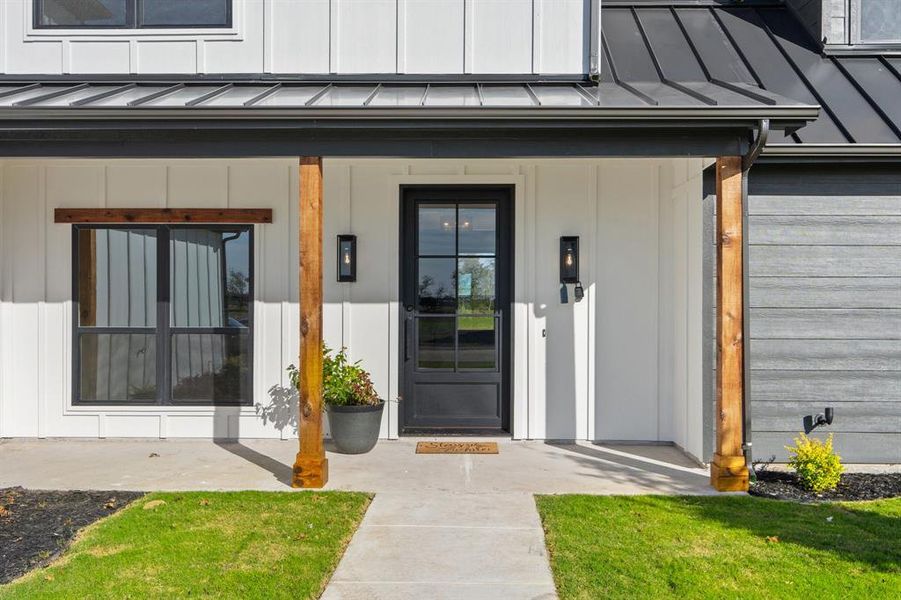 Entrance to property featuring covered porch, board and batten siding, a standing seam roof, and a lawn Entrance to property featuring covered porch, board and batten siding, a standing seam roof, and a lawn