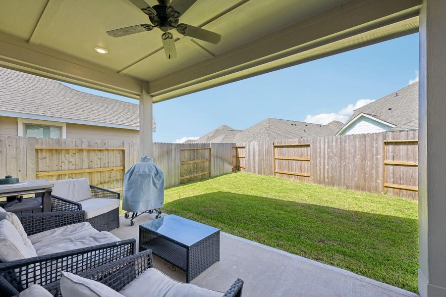 Charming covered patio with comfortable seating overlooks a private, fenced backyard, perfect for relaxation and outdoor gatherings.