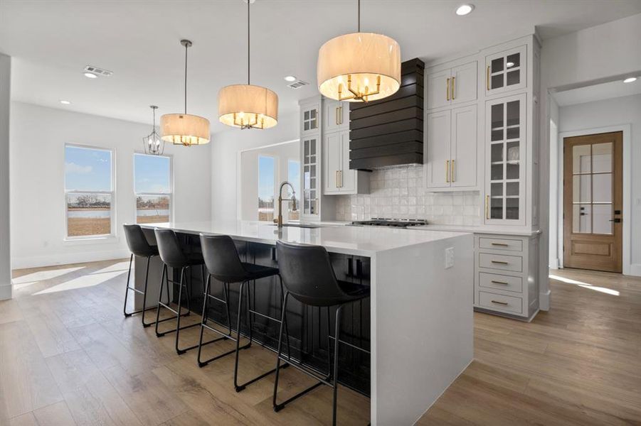 Kitchen with tasteful backsplash, light wood-style floors, visible vents, a spacious island, and a sink Kitchen with tasteful backsplash, light wood-style floors, visible vents, a spacious island, and a sink