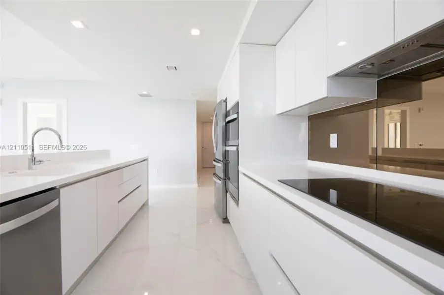 Modern kitchen featuring high-gloss white cabinetry, white stone countertops, integrated stainless steel appliances, a tinted glass backsplash, and polished tile flooring