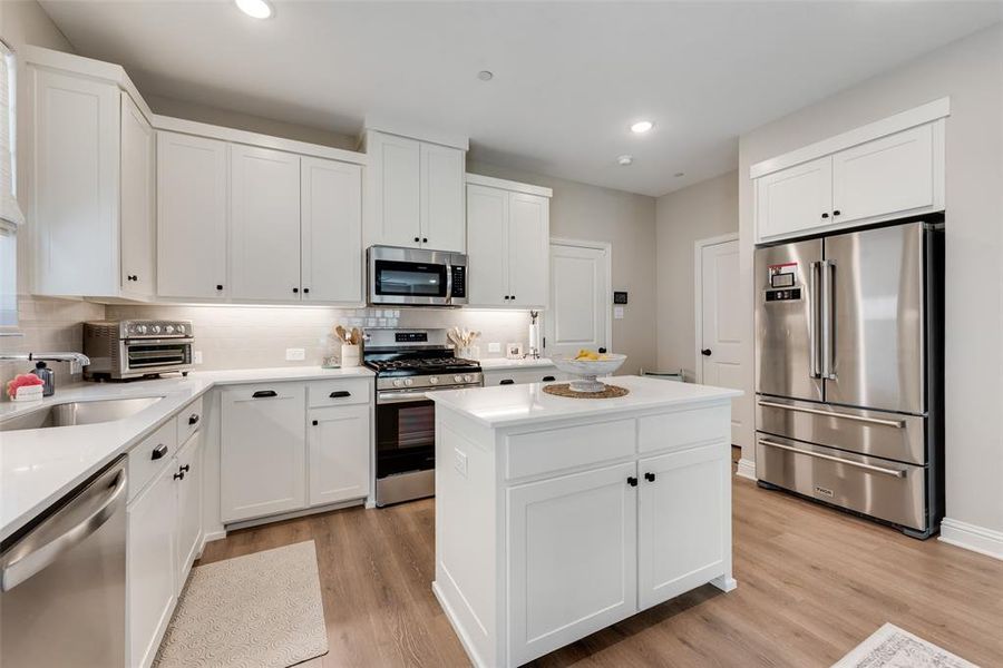 Modern kitchen featuring white shaker cabinetry, stainless steel appliances, a center island, upgraded Pergo water tight laminate wood look flooring, and recessed lighting Modern kitchen featuring white shaker cabinetry, stainless steel appliances, a center island, upgraded Pergo water tight laminate wood look flooring, and recessed lighting