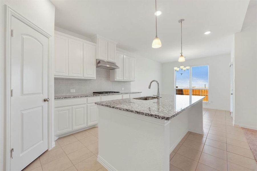 Kitchen featuring an island with sink, light stone countertops, white cabinets, extractor fan, and hanging light fixtures