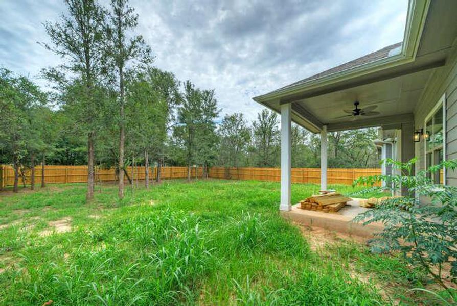 Fenced backyard with ceiling fan and view of wooded area