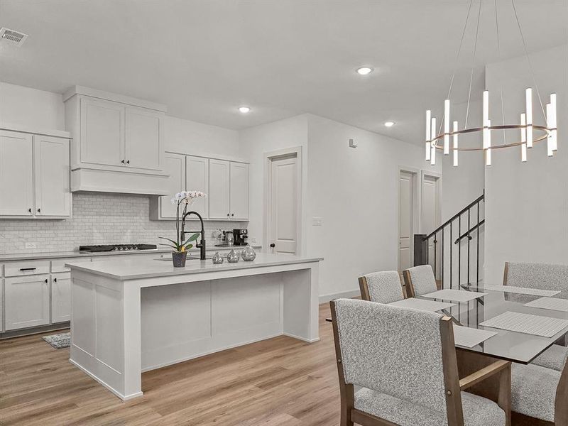 Kitchen with a chandelier, decorative light fixtures, a center island with sink, light hardwood / wood-style floors, and white cabinets