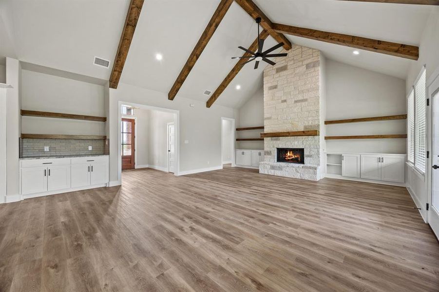 Unfurnished living room featuring high vaulted ceiling, ceiling fan, a fireplace, light wood finished floors, and beamed ceiling Unfurnished living room featuring high vaulted ceiling, ceiling fan, a fireplace, light wood finished floors, and beamed ceiling