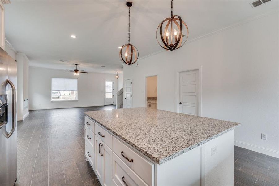 Kitchen with stainless steel refrigerator with ice dispenser, light stone counters, ceiling fan with notable chandelier, pendant lighting, and white cabinets