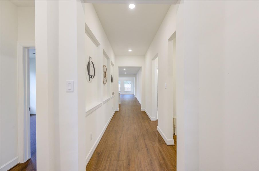 This hallway showcases a bright, spacious hallway with wood flooring and recessed lighting, leading to an open area. Walls are adorned with decorative niches, adding a touch of elegance.