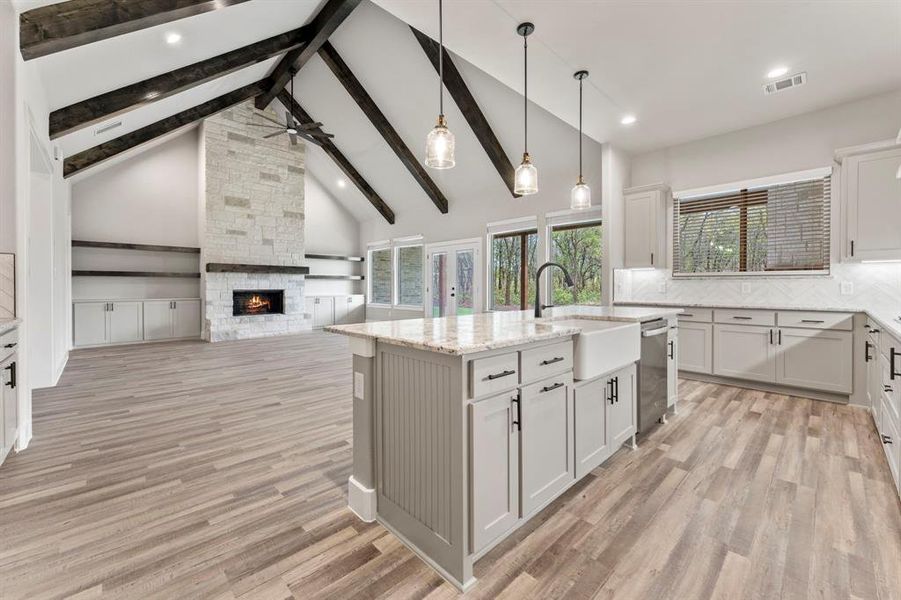 Kitchen with light hardwood / wood-style floors, a center island with sink, dishwasher, tasteful backsplash, and a fireplace