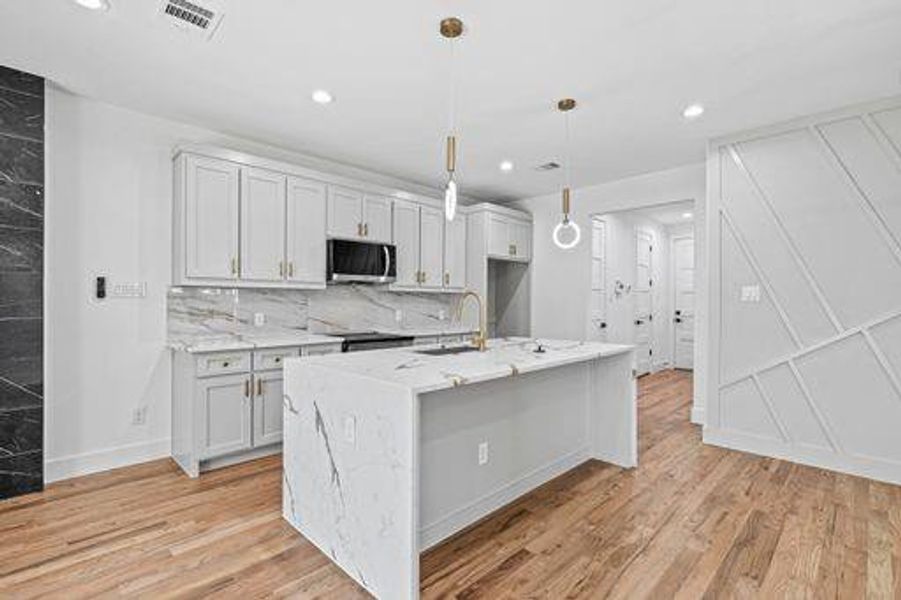 Kitchen with sink, light stone countertops, light wood-type flooring, an island with sink, and decorative light fixtures