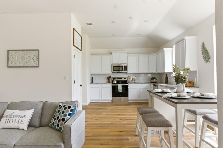 Kitchen featuring stainless steel appliances, white cabinets, light wood-style floors, a peninsula, and backsplash