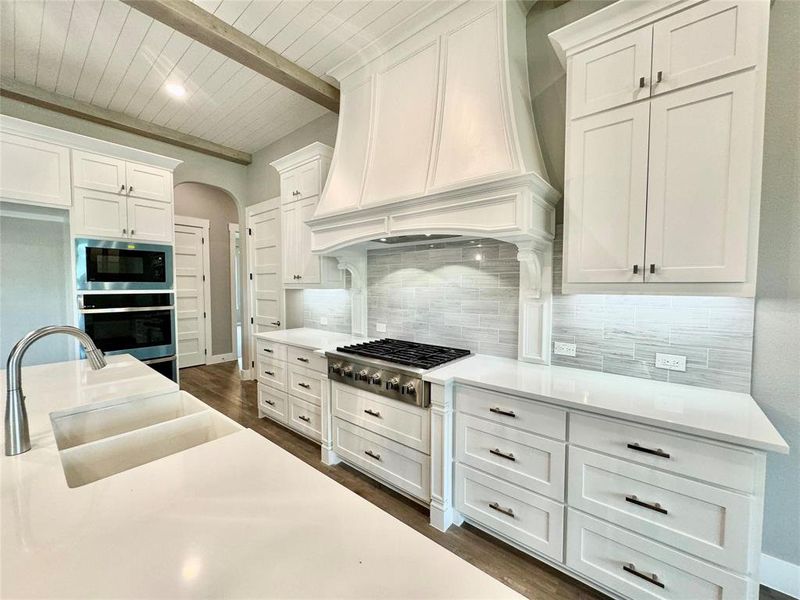Kitchen featuring stainless steel appliances, premium range hood, wooden ceiling with exposed beams, a sink, and white cabinets