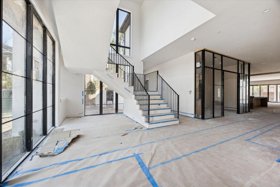 Grand staircase entry featuring modern iron railings and expansive floor to ceiling windows that flood the space with natural light. The open design connects both levels seamlessly, highlighting clean architectural lines and the homes contemporary aesthetic.