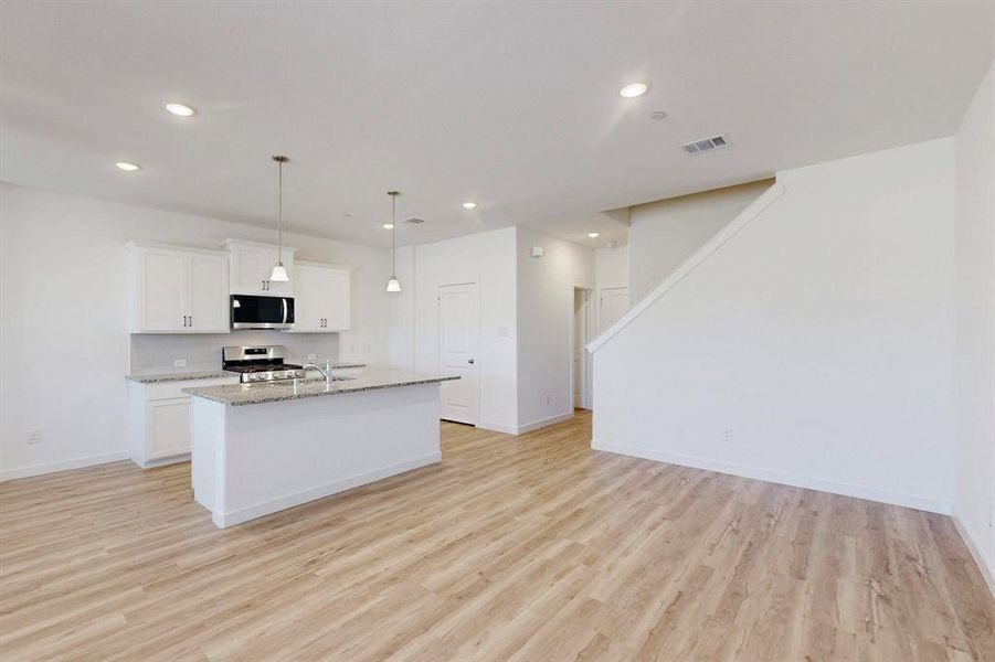 Kitchen featuring an island with sink, hanging light fixtures, white cabinetry, light wood finished floors, and light stone countertops