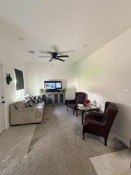 Cozy living room with neutral tones. The room has carpeted flooring, ceiling fan, and a bright window , creating a welcoming atmosphere.