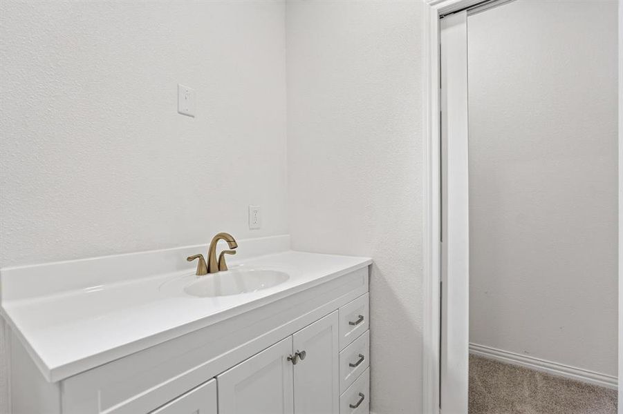 Vanity featuring a white countertop with integrated sink and brass-finish faucet