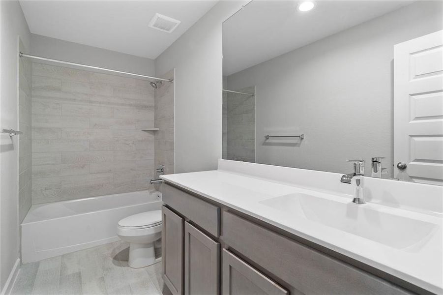 Secondary bath features tile flooring, bath/shower combo with tile surround, white stained wood cabinets, beautiful light countertops, mirror, sleek fixtures and modern finishes.