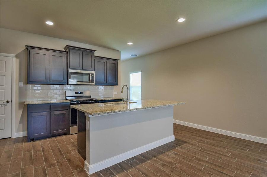 Kitchen featuring appliances with stainless steel finishes, dark wood finished floors, backsplash, an island with sink, and recessed lighting Kitchen featuring appliances with stainless steel finishes, dark wood finished floors, backsplash, an island with sink, and recessed lighting