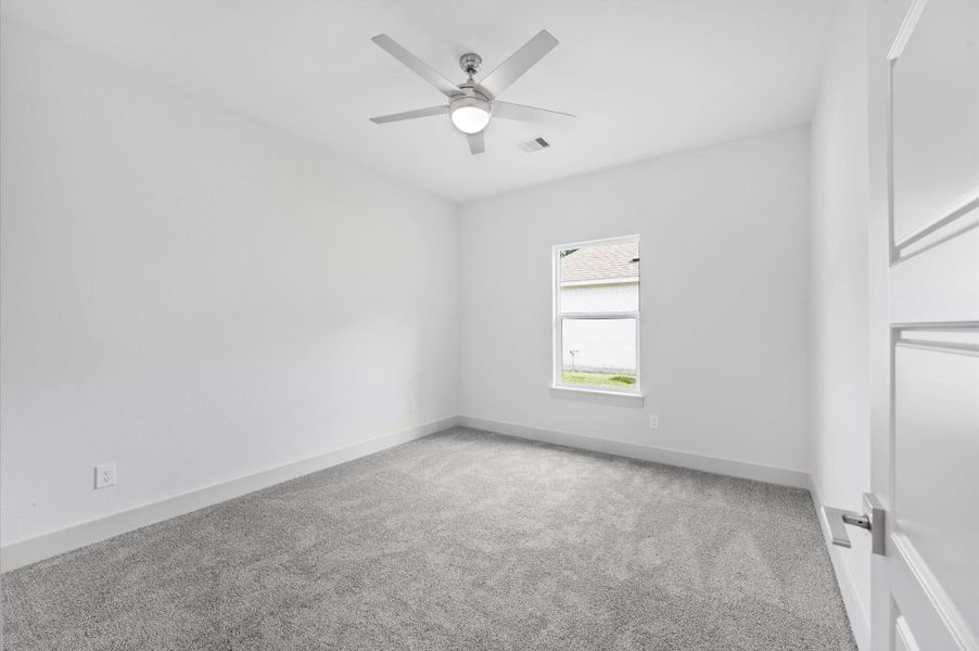 This is a bright, unfurnished bedroom featuring neutral walls and carpeting. It includes a ceiling fan and a window providing natural light. This is a bright, unfurnished bedroom featuring neutral walls and carpeting. It includes a ceiling fan and a window providing natural light.