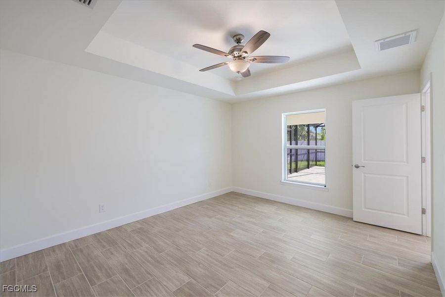 Spare room with a raised ceiling, wood finish floors, and a ceiling fan
