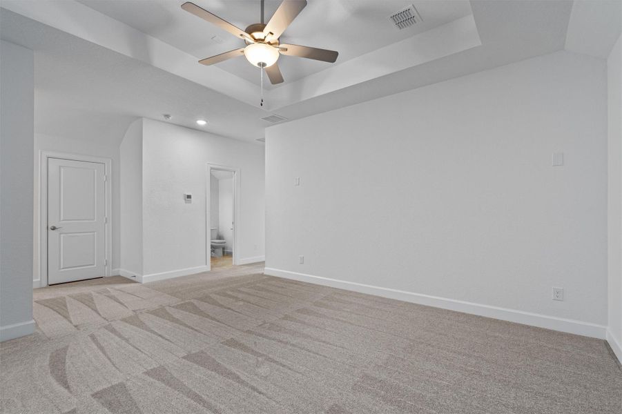 Spacious room featuring tray ceilings, neutral carpeting with abstract patterns, recessed lighting, and a ceiling fan with integrated light fixture