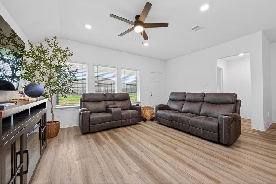 Bright living room with modern laminate flooring, a ceiling fan, and large windows providing ample natural light.